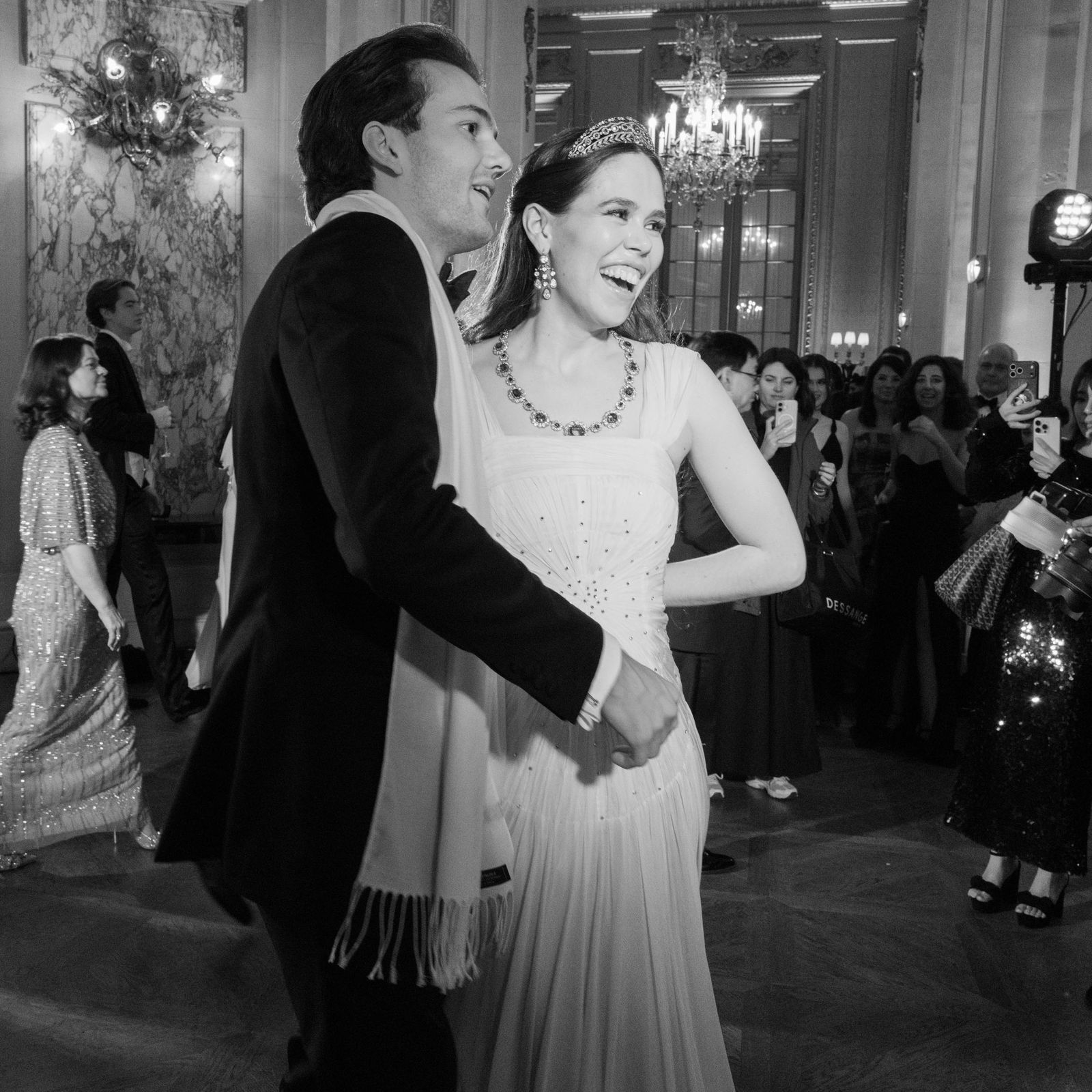 התמונה עשויה להכיל בגדים אביזרי שמלה תכשיטים שרשרת לבוש רשמי חליפת נברשת מנורת מבוגר ואדם