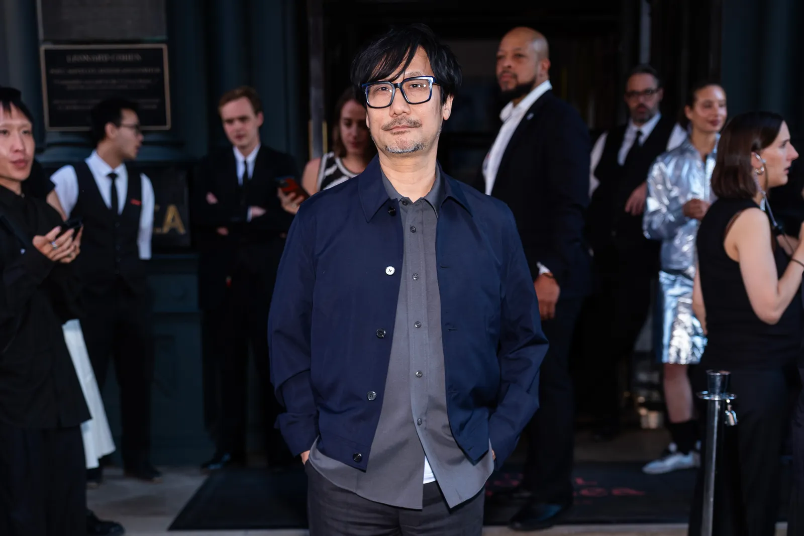 התמונה עשויה להכיל Hideo Kojima בלייזר מעיל מעיל אדם מבוגר פנים שמח ראש חיוך ואביזרים